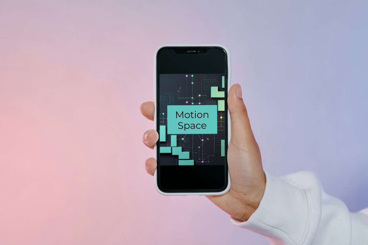 A hand wearing a white long-sleeve shirt holds a smartphone displaying the 'Motion Space' app logo against a soft pink and purple gradient background.